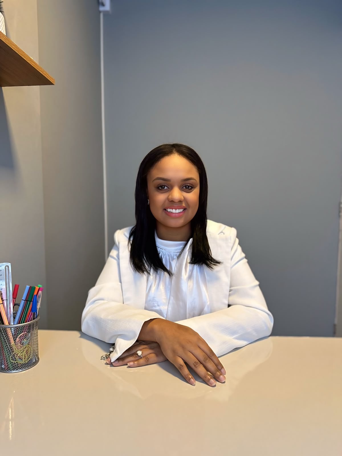 Andressa Gabrielle Frutuoso de blazer branco, sentada à mesa do consultório